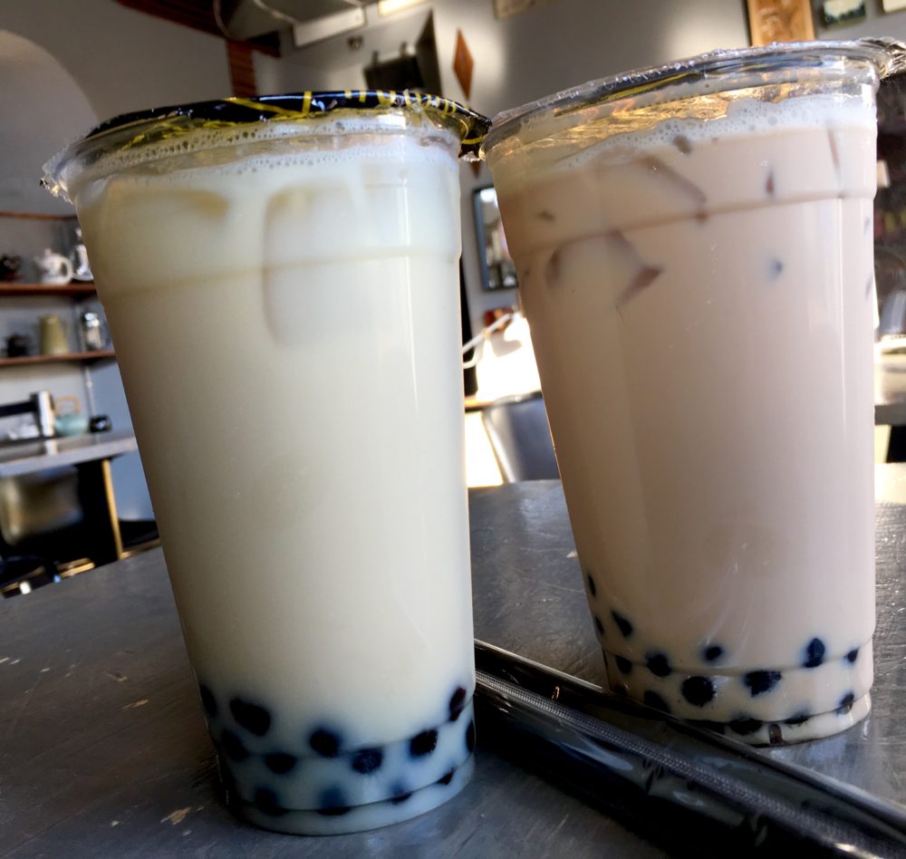 Two cups of light brown bubble tea with black tapioca boba balls in the bottom of each, with two black straws in between the cups. Located at Honey Bubble Tea in the Virginia Highlands neighborhood of Atlanta Georgia