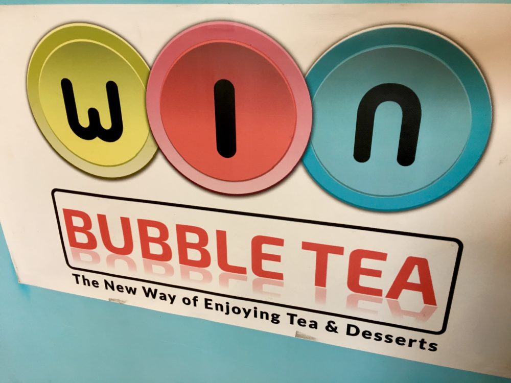 A white wall poster hanging on a turquoise wall with green, pink, and turquoise blue circles with the logo for WIN Bubble Tea in Nashville, Tennessee