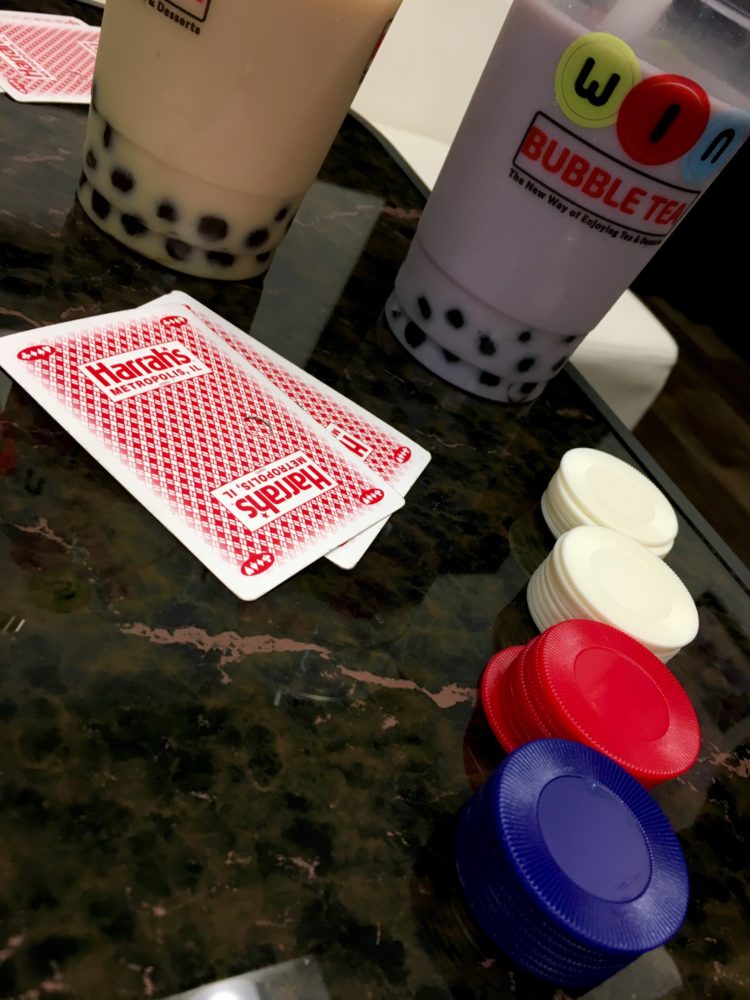 Purple Taro Bubble Tea and a Cream Colored WIntermelon Bubble Tea are in the background, with red Harrah's Casino poker playing cards and red, white, and blue round poker chips in the foreground. This is on the table in the game lounge of WIN Bubble Tea in Nashville, Tennessee
