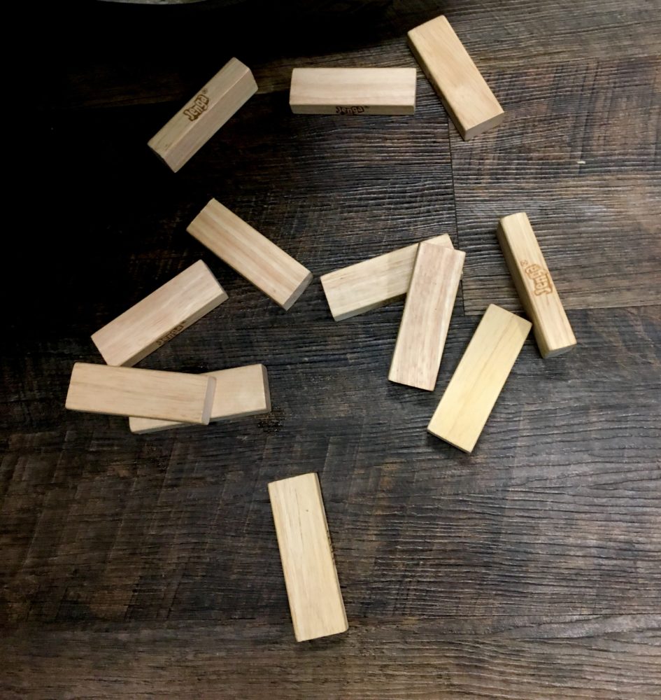 Wooden rectangular JENGA game pieces spread across a grey woodgrain table in the game lounge of red Harrah's Casino poker playing cards and red, white, and blue round poker chips in the foreground. This is on the table in the game lounge of WIN Bubble Tea in Nashville, Tennessee