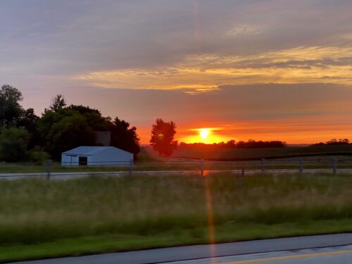 A gray interstate driving towards a Golden Orange Sunset with Pinkish Blue Clouds on the horizon