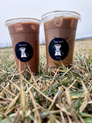 Two iced blackberry lattes from Java Drip in Clarkrange TN sitting in a field of green grass against an overcast sky